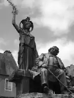 Description de l'image par IA : Statue d'Ernest Renan à Tréguier. Homme assis, femme debout tenant une couronne.